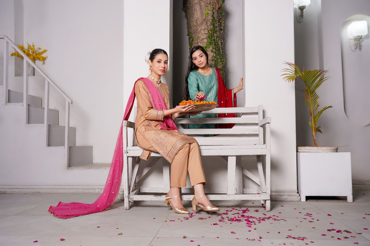 Two women in traditional Pakistani clothing pose elegantly indoors.